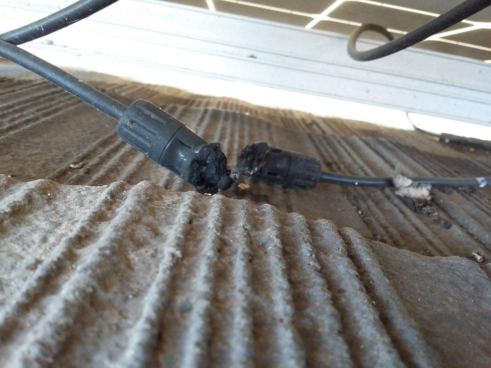 Two black extension cords with melted connectors on a dusty, ribbed surface, showing burn damage and potential hazard, underneath a ceiling grid.
