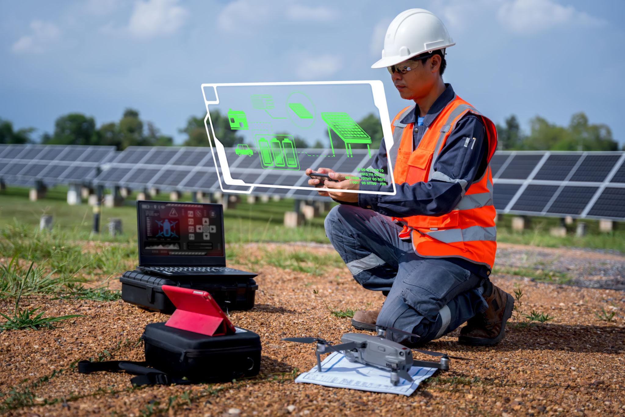 Worker in safety gear using a tablet with a holographic AR display over a solar farm, drones and laptops visible nearby (informational).